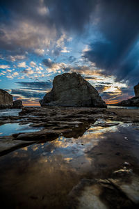 Rocks on sea shore against sky during sunset