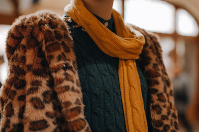 Mannequin wearing a green knitted sweater, leopard fur coat and a cozy yellow scarf. 