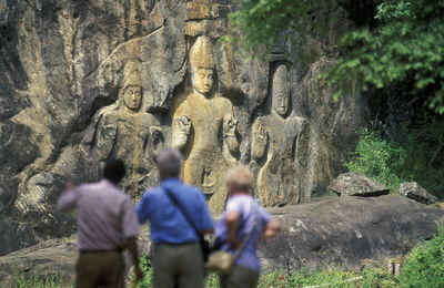 Tourists visiting buduruvagala against buddha carvings on rock