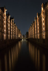 Illuminated buildings by river against sky at night