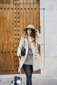 Young woman wearing hat standing against wall