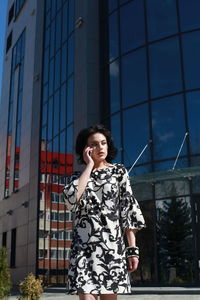 Fashionable young woman wearing floral patterned dress standing against building in city