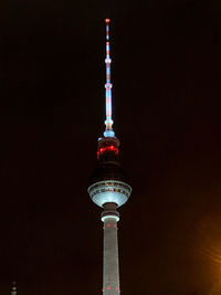 Low angle view of communications tower and buildings in city at night