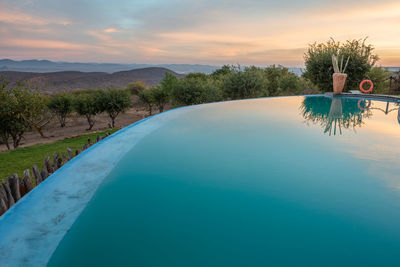 Swimming pool by lake against sky during sunset