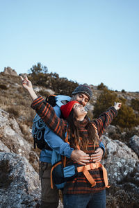 Young couple standing on rock against sky