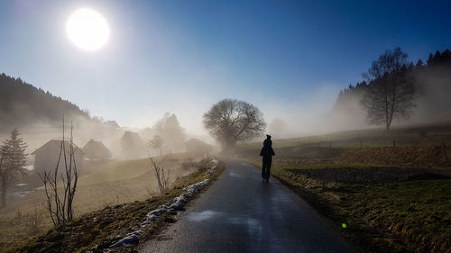 Silhouette man carrying child on road against clear blue sky