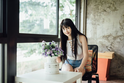 Portrait of young woman sitting on table by window