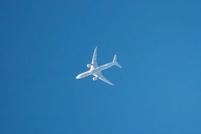 Low angle view of airplane flying against clear blue sky