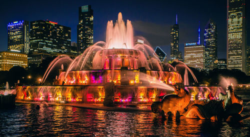 Illuminated buckingham fountain against skyscrapers at night