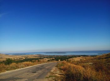 Road by sea against clear blue sky