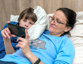 Woman using smart phone while lying with son on bed