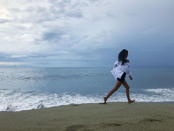 Full length of woman walking at beach against sky