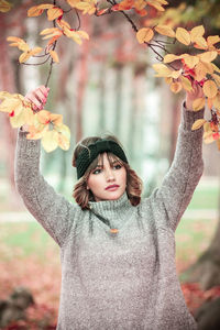 Young woman looking away while holding branches at public park