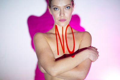 Portrait of young woman standing against pink background