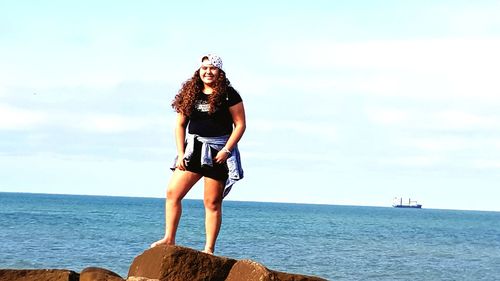 Portrait of girl standing on rock by sea against sky