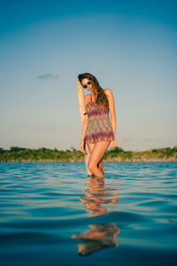 Woman standing in sea against clear blue sky