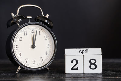 Close-up of clock with calendar on table against black background