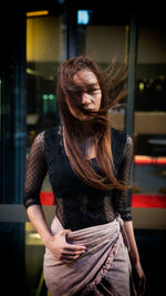 Portrait of female model with tousled hair standing against store