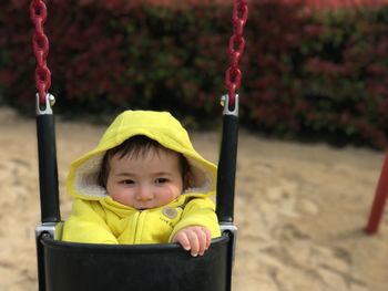 Cute baby wearing yellow warm clothing on swing at playground