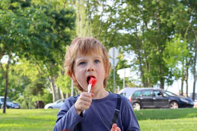 The blond boy holds a fork in his hand and eats a watermelon. a five-year-old boy narrows his eyes  