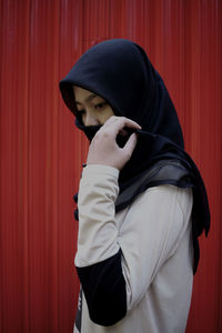 Woman wearing hijab standing against red curtain