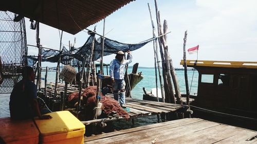 Fisherman standing by fishing net on jetty at harbor against sky