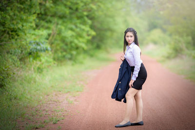 Full length of smiling young woman against trees