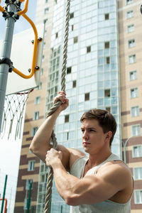 Young man holding rope against building