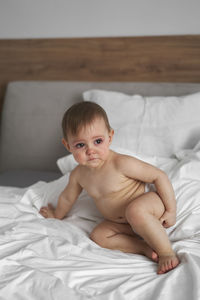 Shirtless baby girl sitting on be