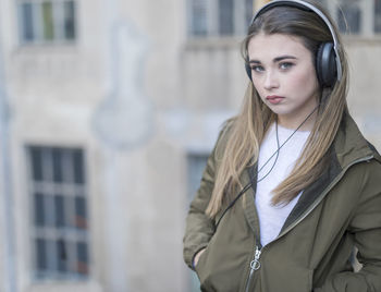 Close-up portrait of young woman listening music with hands in pocket