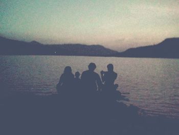 Rear view of people sitting on lakeshore