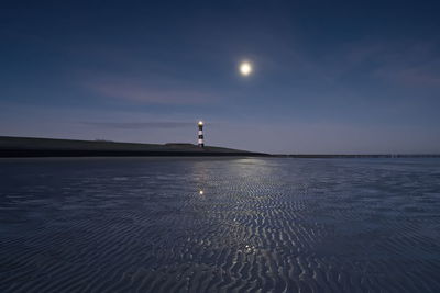 Lighthouse by sea against sky at night