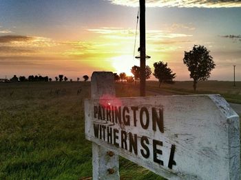 Road sign on grassy field against sky at sunset