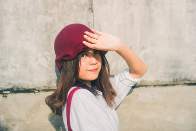 Portrait of young woman in hat standing against wall