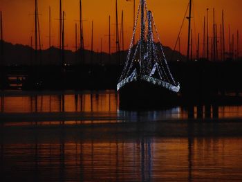 Illuminated boat on river against sky during sunset