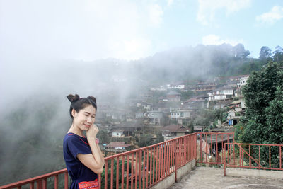 Happy woman with eyes closed standing at observation point during foggy weather