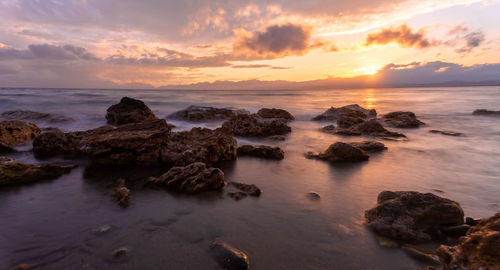 Rocks on shore against sky during sunset