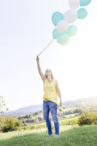 Full length of woman holding balloons against clear sky
