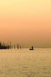 Silhouette man in boat on sea against clear sky during sunset