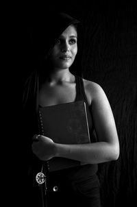 Portrait of young woman standing against black background