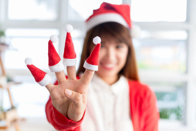 Close-up of woman wearing santa hats in fingers