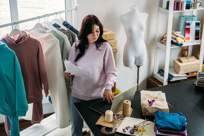 Young woman tailor fashion designer dressmaker using laptop in seamstress studio