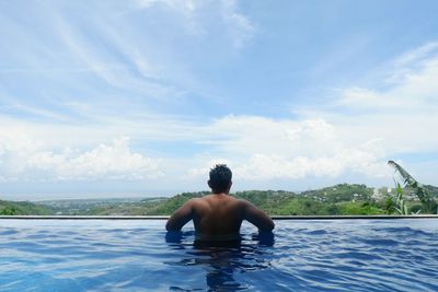 Full length of shirtless man in swimming pool against sea