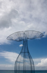 Metallic structure in the shape of a whale's tail on a background of blue sky