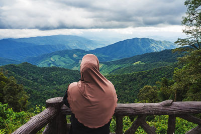 Rear view of woman standing by railing against mountains and sky