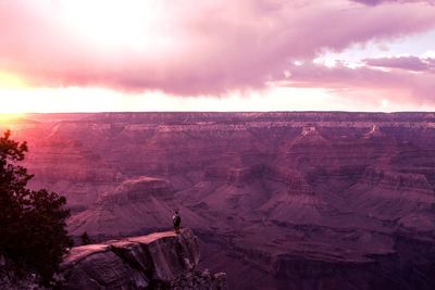 Rear view of man standing on cliff against sky during sunset