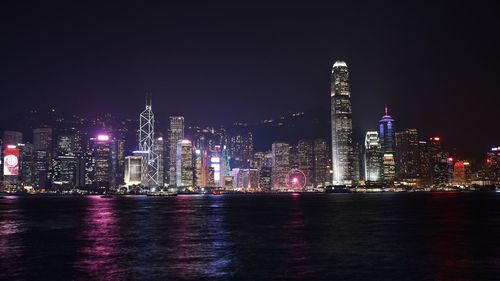 Illuminated buildings by river against sky at night