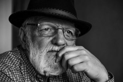 Close-up of thoughtful senior man wearing hat and eyeglasses looking away at home