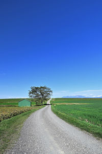 Road amidst field against clear blue sky