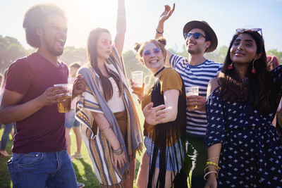 Friends holding beer in glasses while standing on grass